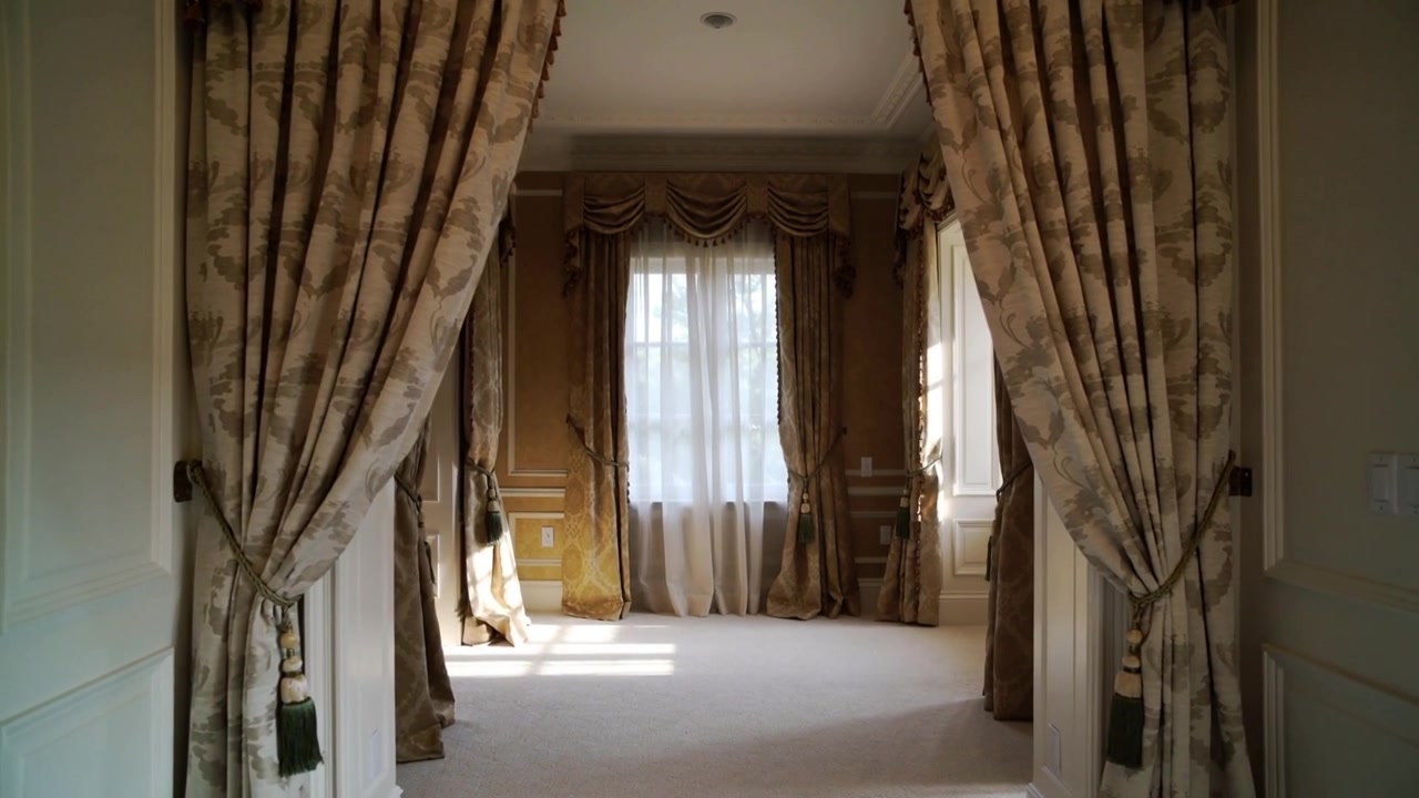 Zooming camera moving toward tall window from hallway, revealing drapes with tassel tiebacks