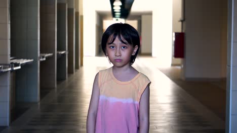 Portrait-of-a-young-Southeast-Asian-boy-alone-scared-looking-into-camera-in-an-abandoned-mall-hallway-with-light-and-shadow-in-the-background