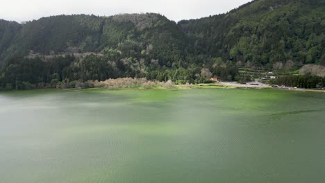 an aerial view captures waters surrounding a shoreline adorned with hills and dense forests, representing the beauty and essence of nature