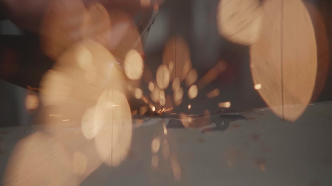 A slow-motion macro shot captures a shower of bright sparks flying as an angle grinder works on a metal surface. A concept of industrial labor, metalwork, and manufacturing