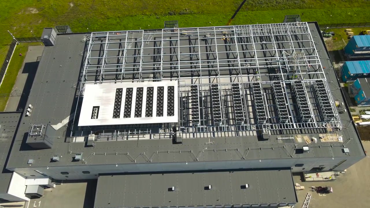 Top-down luftfoto, der flyver over en stor datacenterbygning under opførelse, viser installationen af kraftige kølesystemer og ventilationsudstyr på det moderne flade tag.