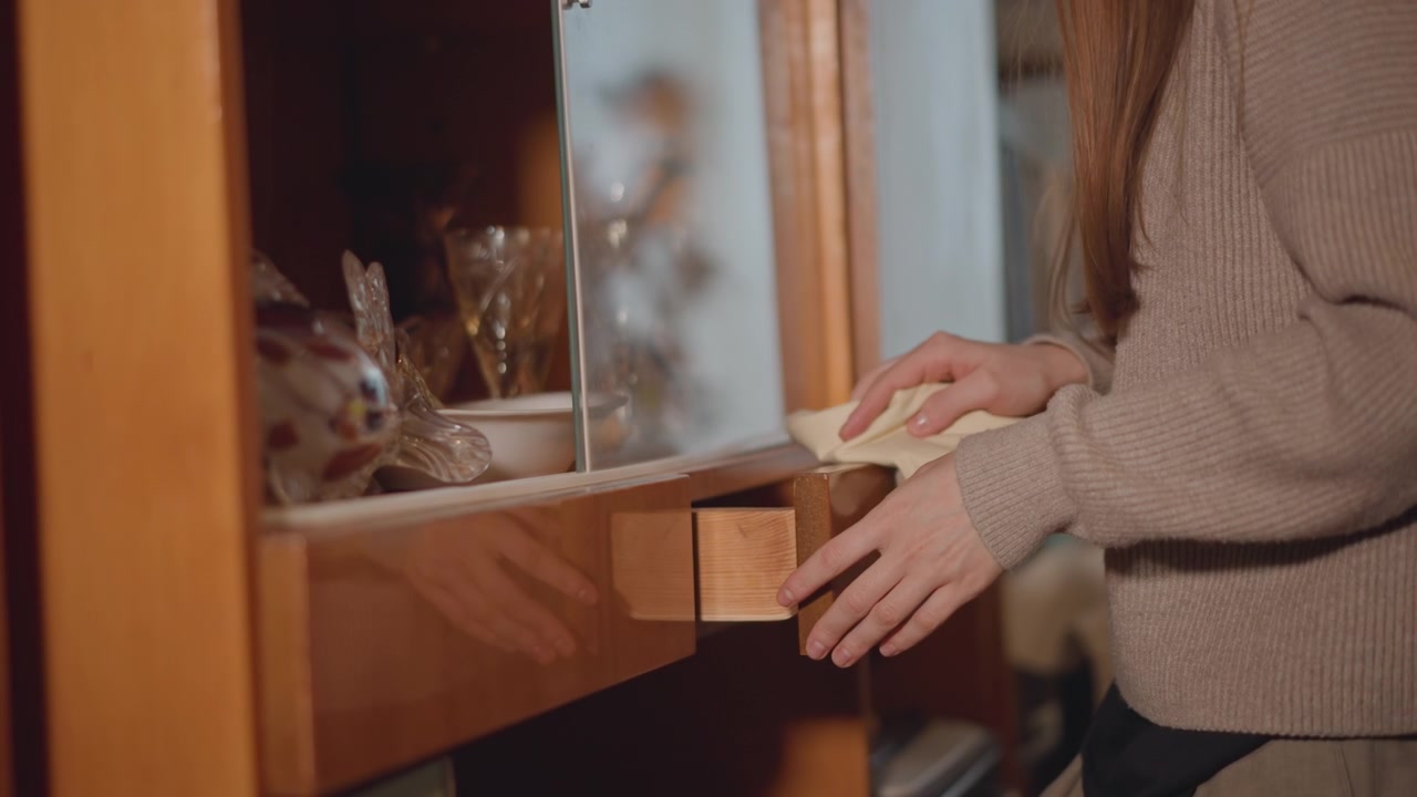 Woman hands opening wooden drawer revealing napkin and glassware long hair and knit sweater, warm amber lighting, vintage cabinet, gentle cleaning motion hostess prepares table, collector inspects