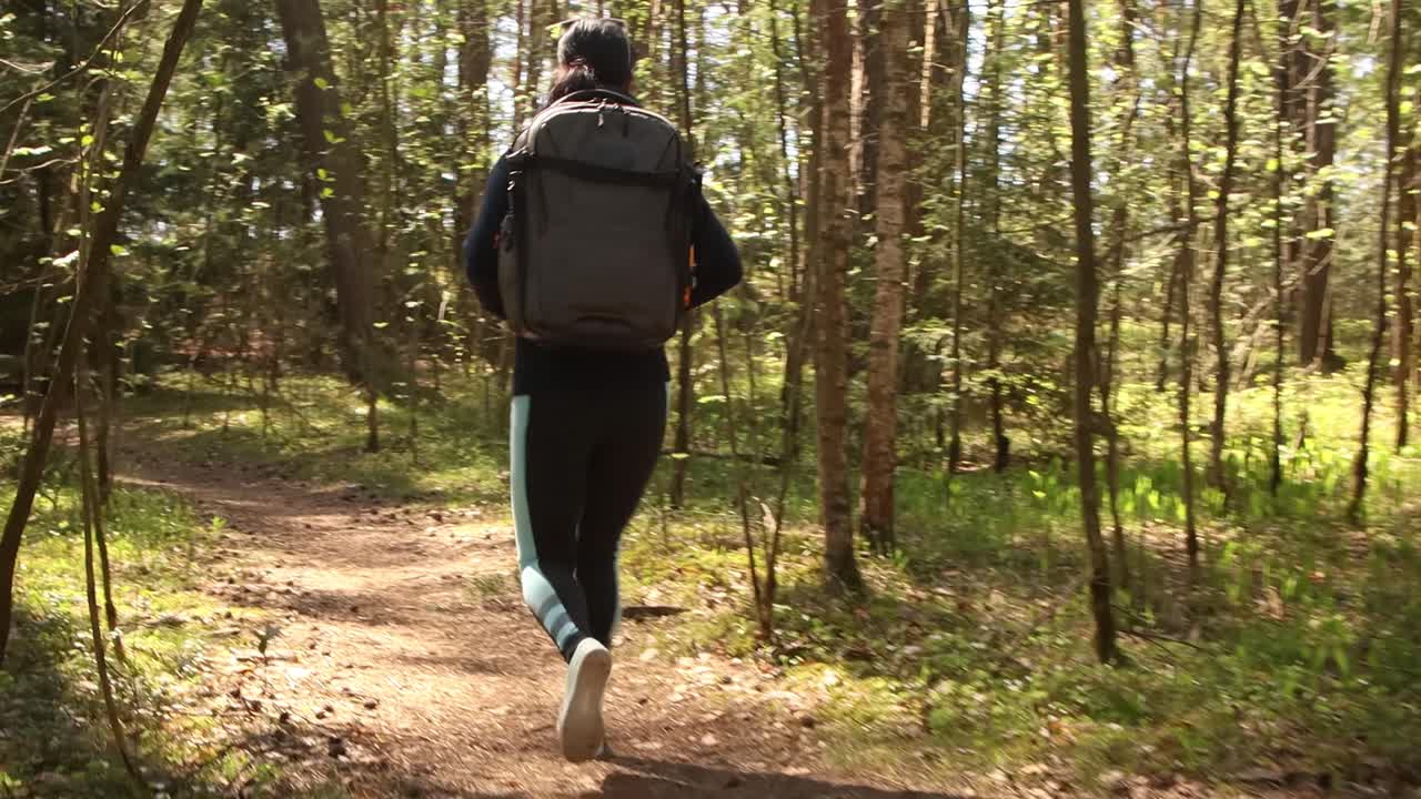 Mulher caminhando com uma mochila de caminhada na floresta verde primavera