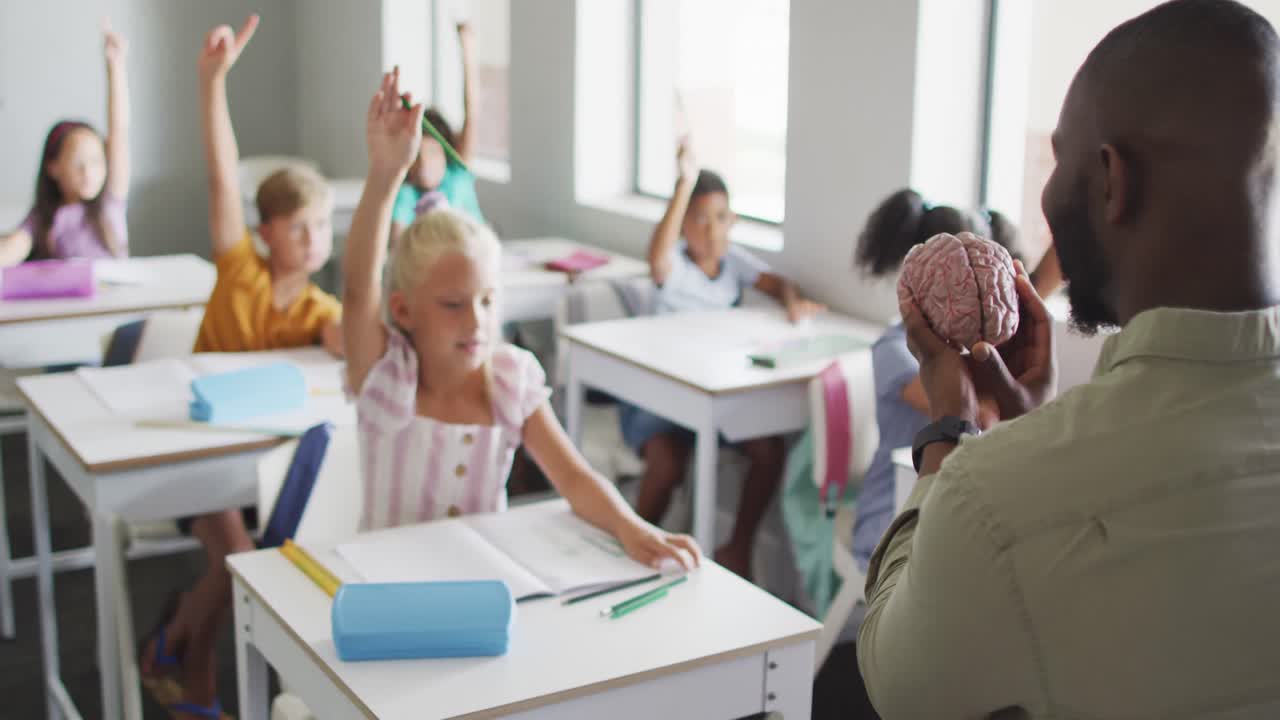 Video of african american male teacher and diverse pupils raising hands during lessons