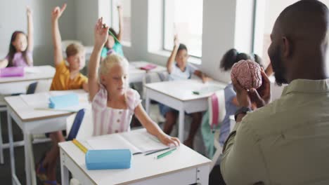video of african american male teacher and diverse pupils raising hands during lessons
