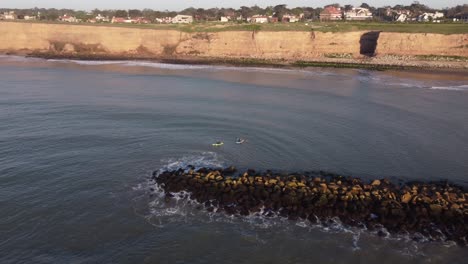 Two-rowers-paddling-in-kayak-in-Atlantic-Ocean-along-Acantilados-cliff-and-breakwater,-Mar-del-Plata-in-Argentina