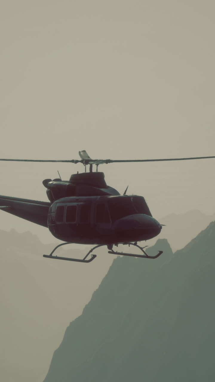 Helicopter flying through mountain range at dusk with misty backdrop