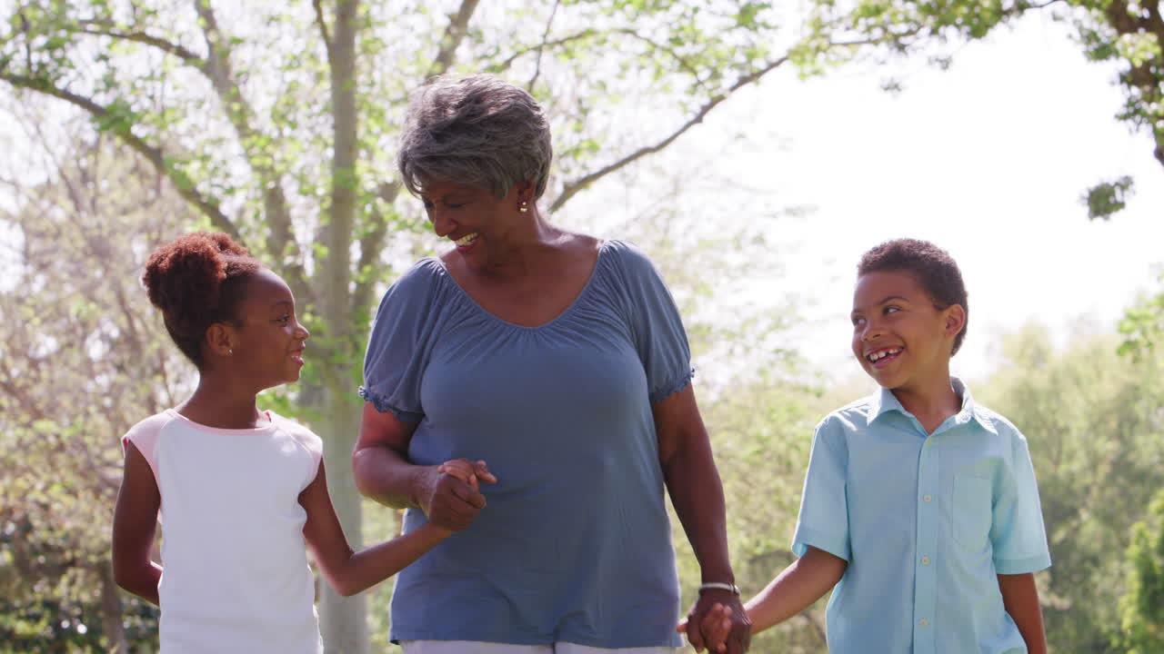 Grandmother Walking In Park And Holding Hands With Grandchildren