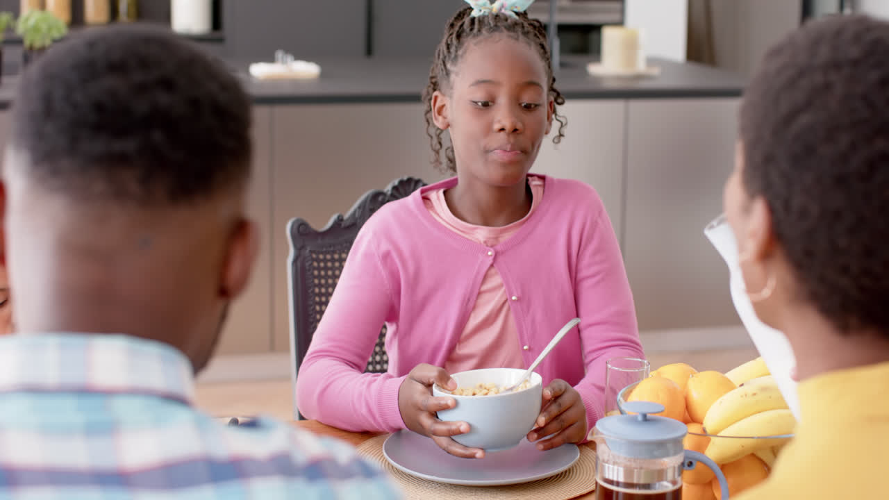 African american parents and daughter eating breakfast at table in kitchen, slow motion