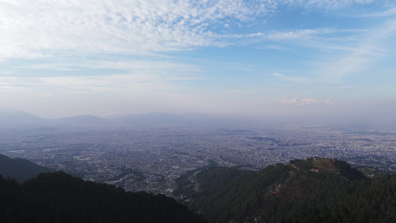 drone view of Kathmandu Valley revealing its dense urban layout, surrounding green hills, and distant Himalayan horizon, capturing the unique blend of culture, terrain, and city life in Nepal