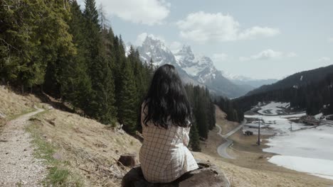 Junge-Frau-Sitzt-Auf-Einem-Baumstumpf-In-Den-Bergen-Mit-Blick-Auf-Die-Dolomiten-In-Italien