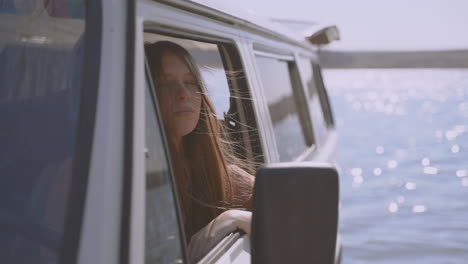 uma jovem ruiva de cabelos compridos sentada em uma caravana à beira de um lago desfruta da natureza e do ar fresco