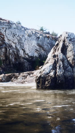 una gran roca se encuentra en un río con montañas en el fondo