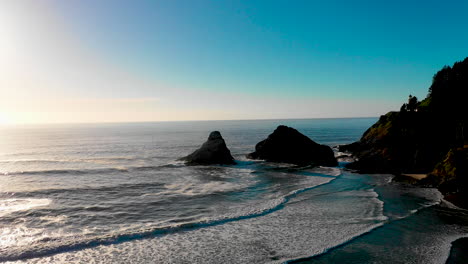 beautiful blue calm waves slowly rolling onto the beach along the coast of oregon and the pacific ocean with blue skies and silhouetted rocks in the background