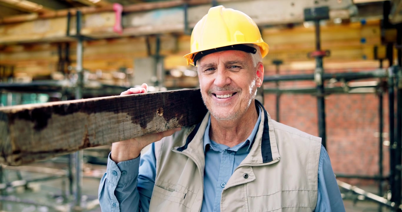 Smiling Mature Construction Worker Carrying Wooden Beam on Shoulder