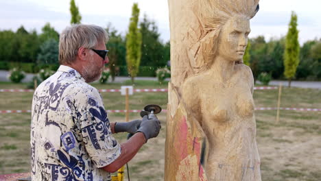 creative process of a female sculpture making. grey-haired man uses electric tool to cut wood.