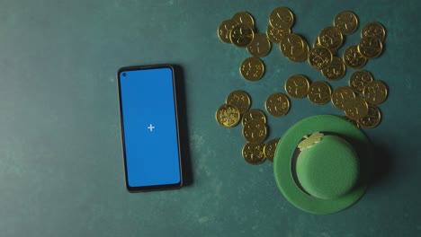 overhead studio shot of green leprechaun top hat with gold coins and blue screen mobile phone to celebrate st patricks day 4