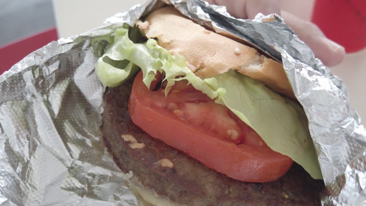 Close up view of burger wrapped in foil showing fresh lettuce, tomato and meat patty