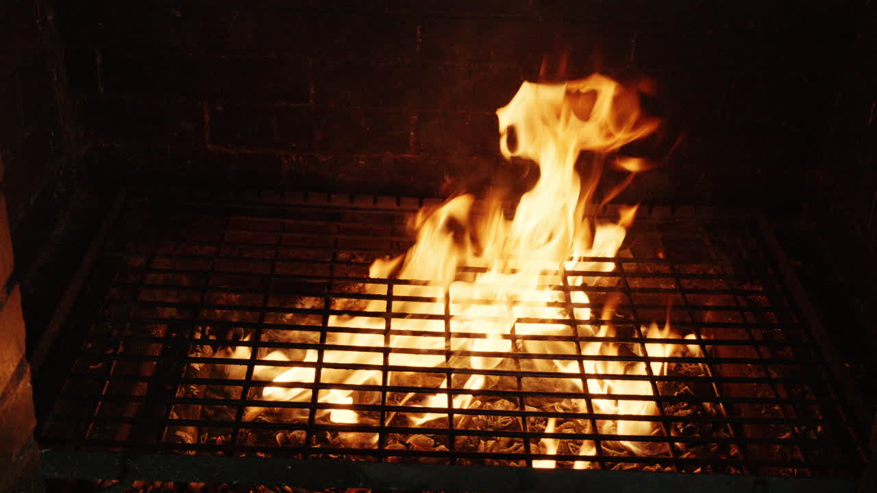 Primo piano di fiamme all'interno di un forno a mattoni o di una griglia con fuoco incandescente e fumo.