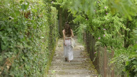 blonde girl in white loose yoga clothes walks on bridge in green forest