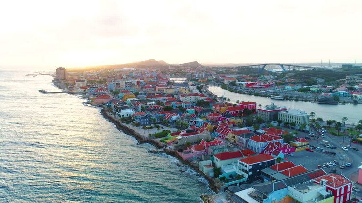 Inquadratura aerea 4K in ascesa che rivela la città di Willemstad e il ponte Regina Giuliana a Curaçao, durante il tramonto all'ora d'oro.