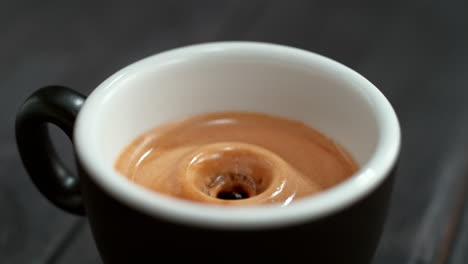 coffee droplet falling into the espresso cup with foamy crema making a splash in macro and slow motion, black background