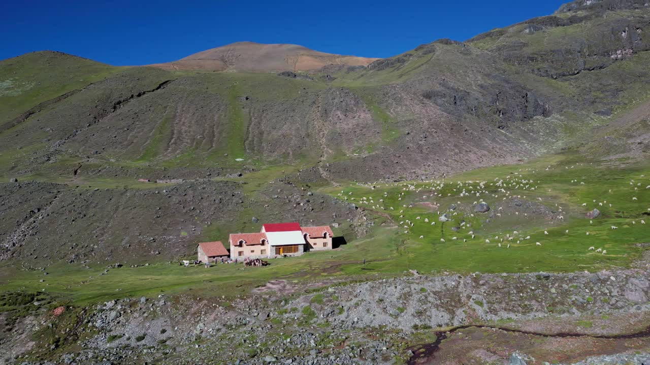 4K aerial footage of a lodge at the foot of Ausangate in the Peruvian Andes. Snowy peaks, grazing llamas, and remote wilderness create a breathtaking setting