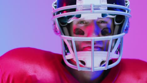 Video-of-portrait-of-caucasian-american-football-player-in-helmet-over-neon-purple-background