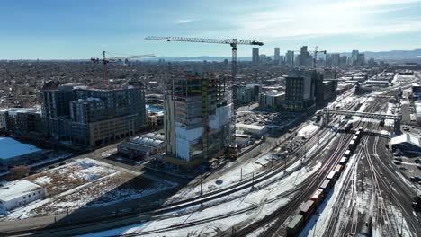 cinematic aerial view of multi story building construction site with view of rail tracks partially covered with snow in foreground and city view in background