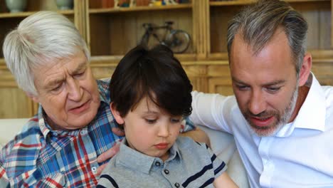 son, father and grandfather sitting on sofa using laptop in living room