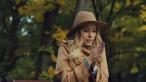 Caucasian-young-blonde-woman-feeling-cold-and-warming-herself-while-she-sitting-on-the-bench-in-the-park-in-autumn