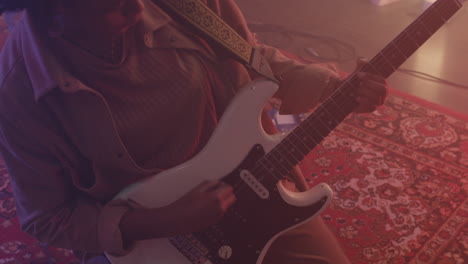 African-american-female-musician-playing-electric-guitar-while-kneeling-on-floor-in-recording-studio