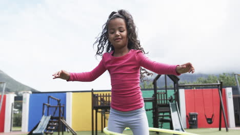 in a school playground, a young african american girl is hula hooping