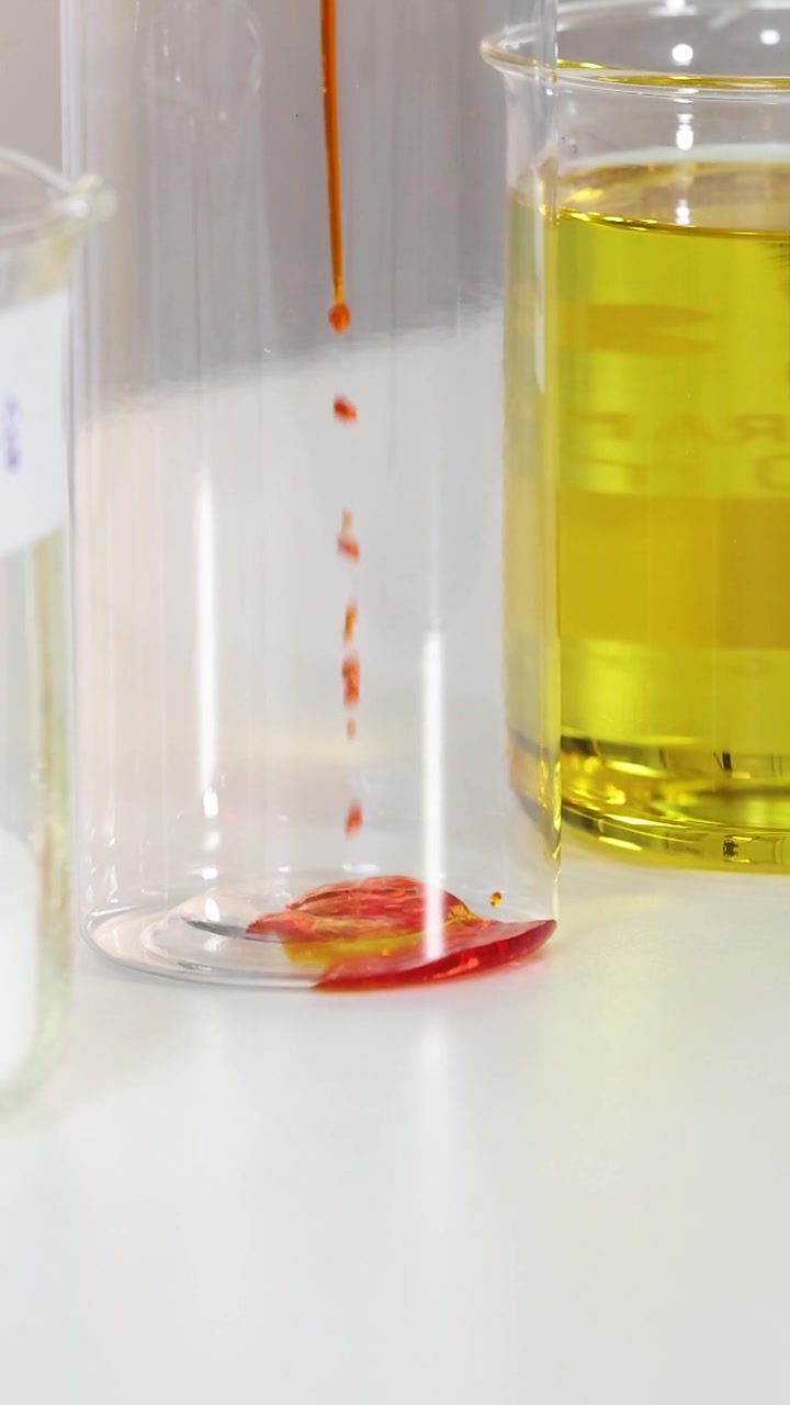 Primo piano verticale di colorante alimentare rosso versato in un becher di vetro trasparente da laboratorio.