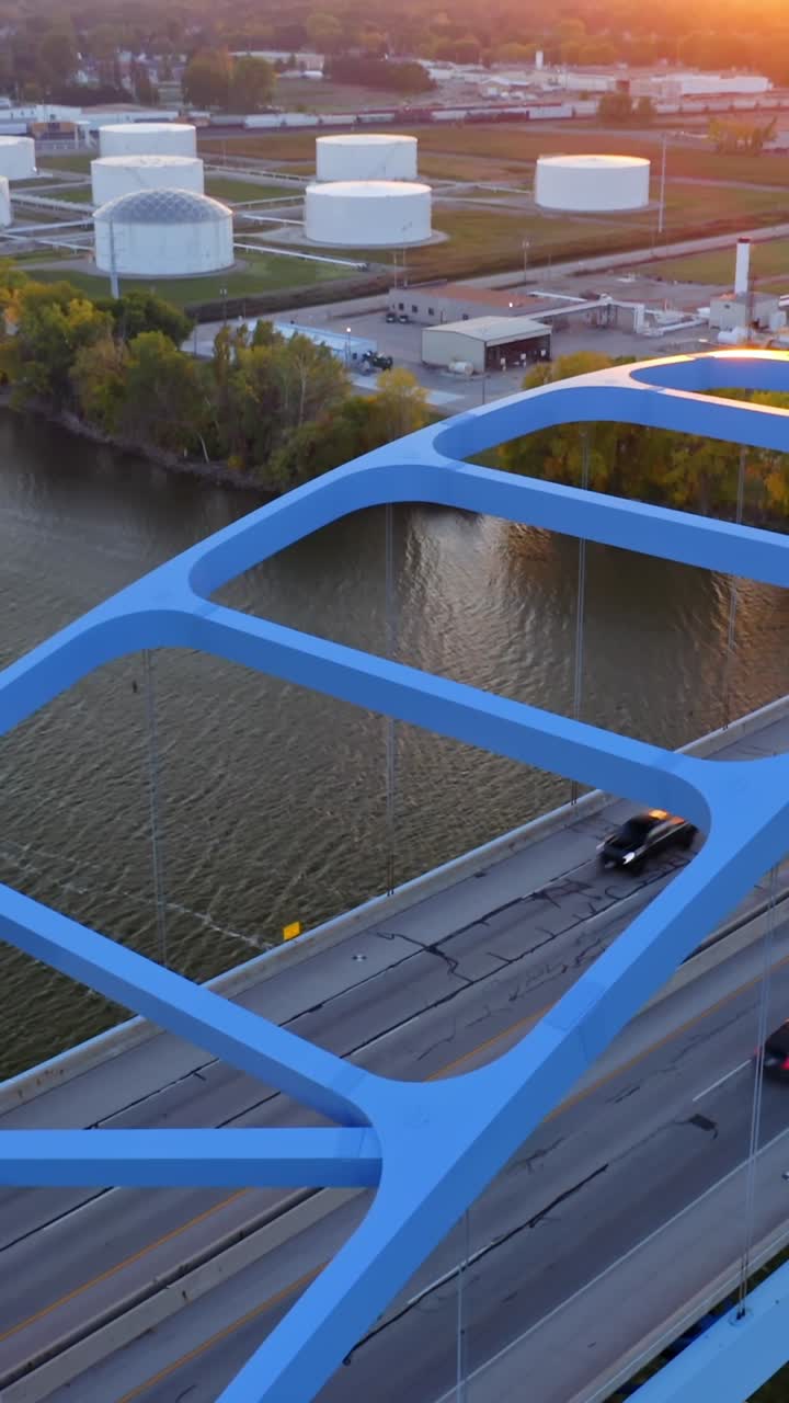 Aerial perspective captures vehicles moving along a steel truss bridge painted bright blue, its geometric framework contrasting sharply against the dark water flowing below