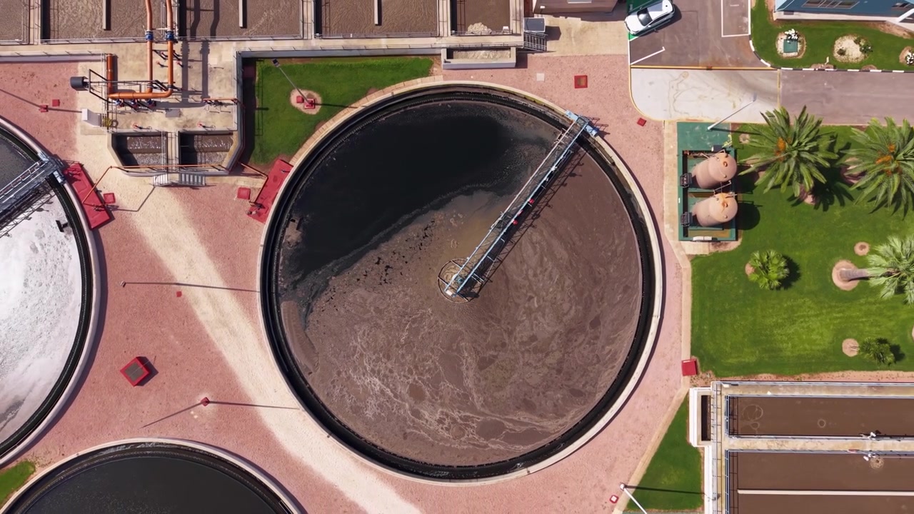 Vista cenital de un tanque clarificador circular en una planta de tratamiento de aguas residuales en España, mostrando el proceso de sedimentación con mecanismo giratorio e infraestructura circundante de la instalación.