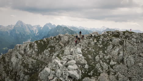 excursionistas parados en las rocas en la cima de la montaña rombon, hermosas montañas vistas en el fondo, la bandera eslovena ondea en la cima