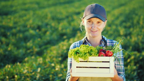 retrato de una agricultora parada en el campo sosteniendo una caja con un conjunto de órganos de verduras frescas