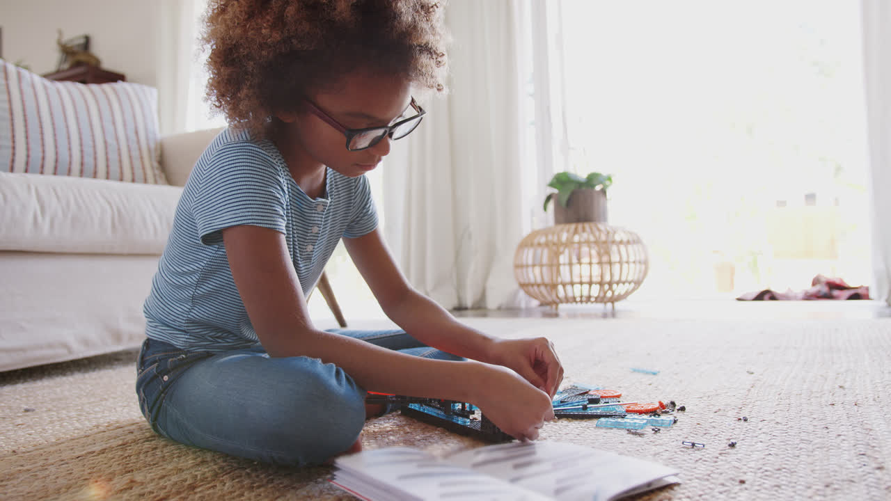 Pre-teen African American girl sitting on the floor in the living room building a construction toy, full length
