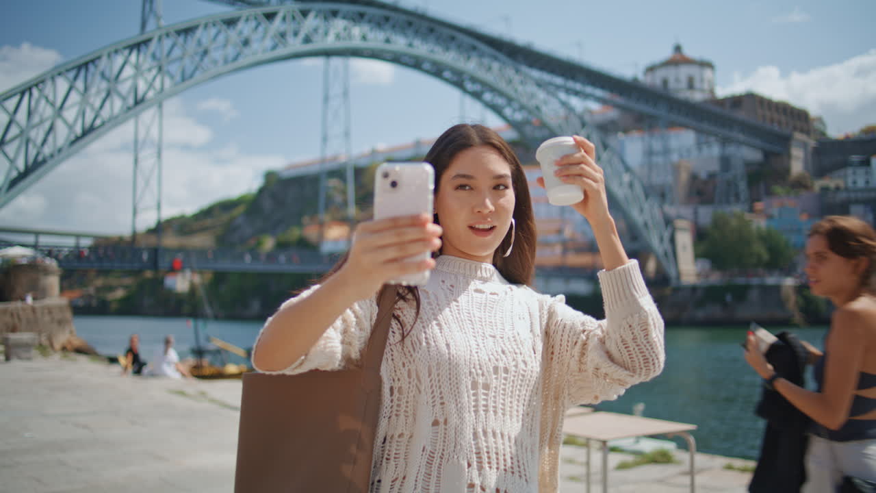 Cheerful blogger holding smartphone recording video at river promenade closeup