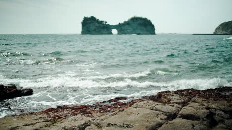 ocean waves hitting the rocky shore overlooking the engetsu island on a sunny day in shirahama, wakayama prefecture, japan