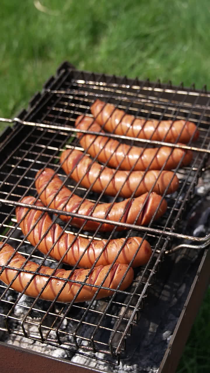 Barbecue grill. Cooking sausages for picnic. Hot dog sausages being cooked and turned over on an outdoor grill. Making a picnic. Vertical video