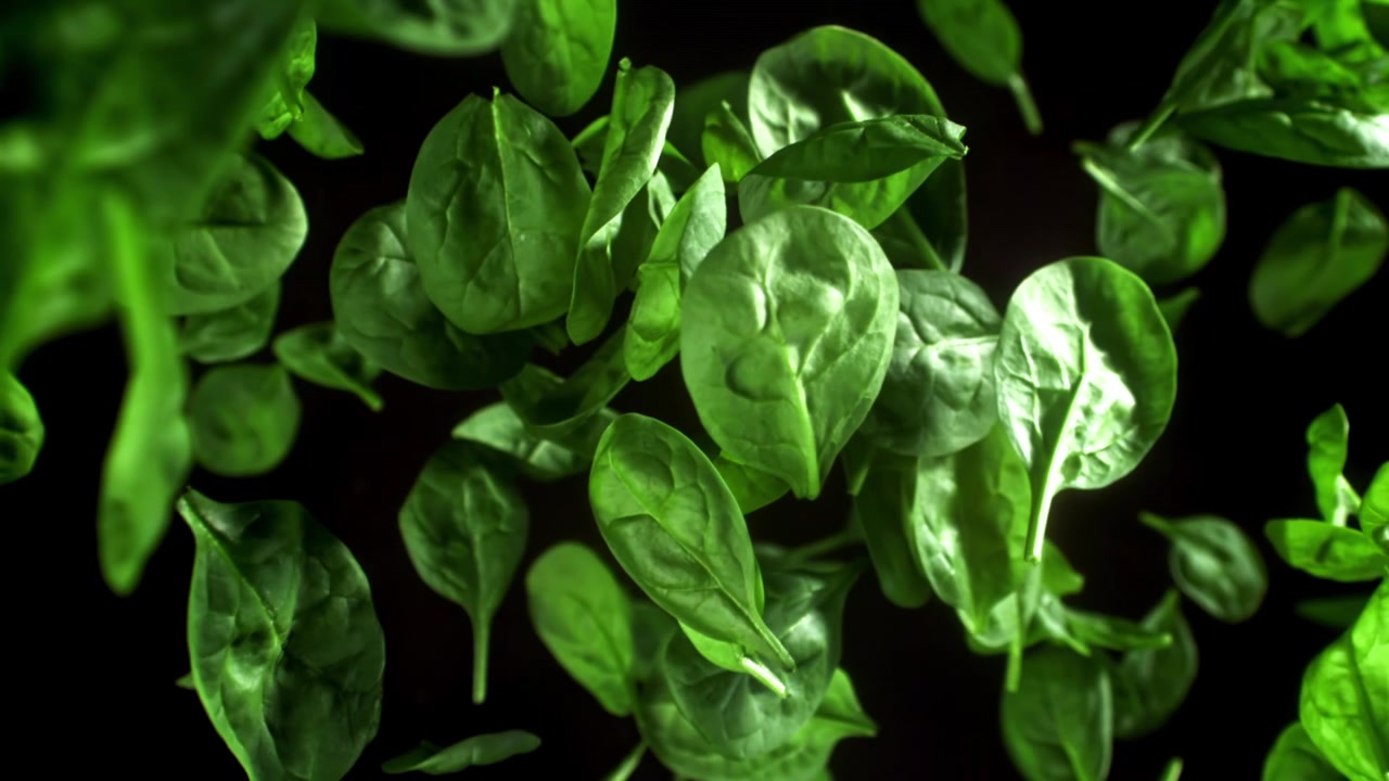 Foglie di spinaci freschi e verdi che cadono al rallentatore su sfondo nero