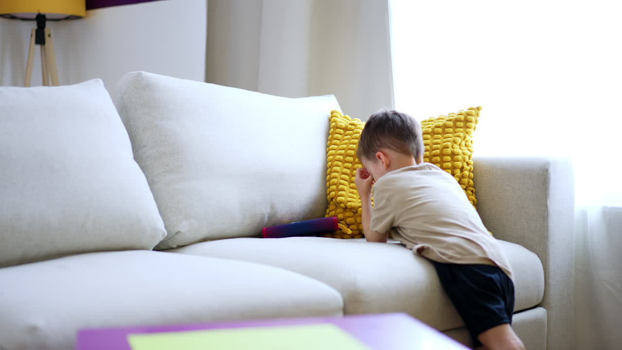 Child quietly plays on sofa. A young boy is focused on a toy while sitting on a cozy sofa in a bright living room