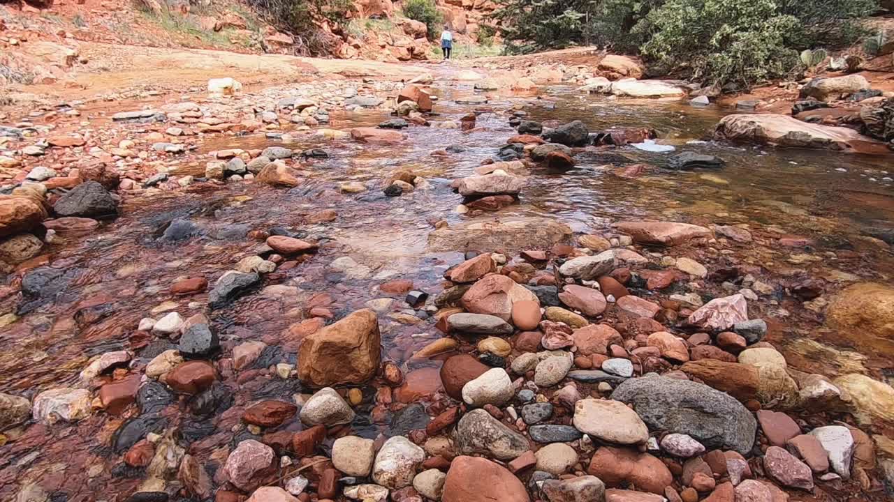 Cold, clean spring runoff washes around multicolor river rock. Hiker in the distance, Sedona, Arizona