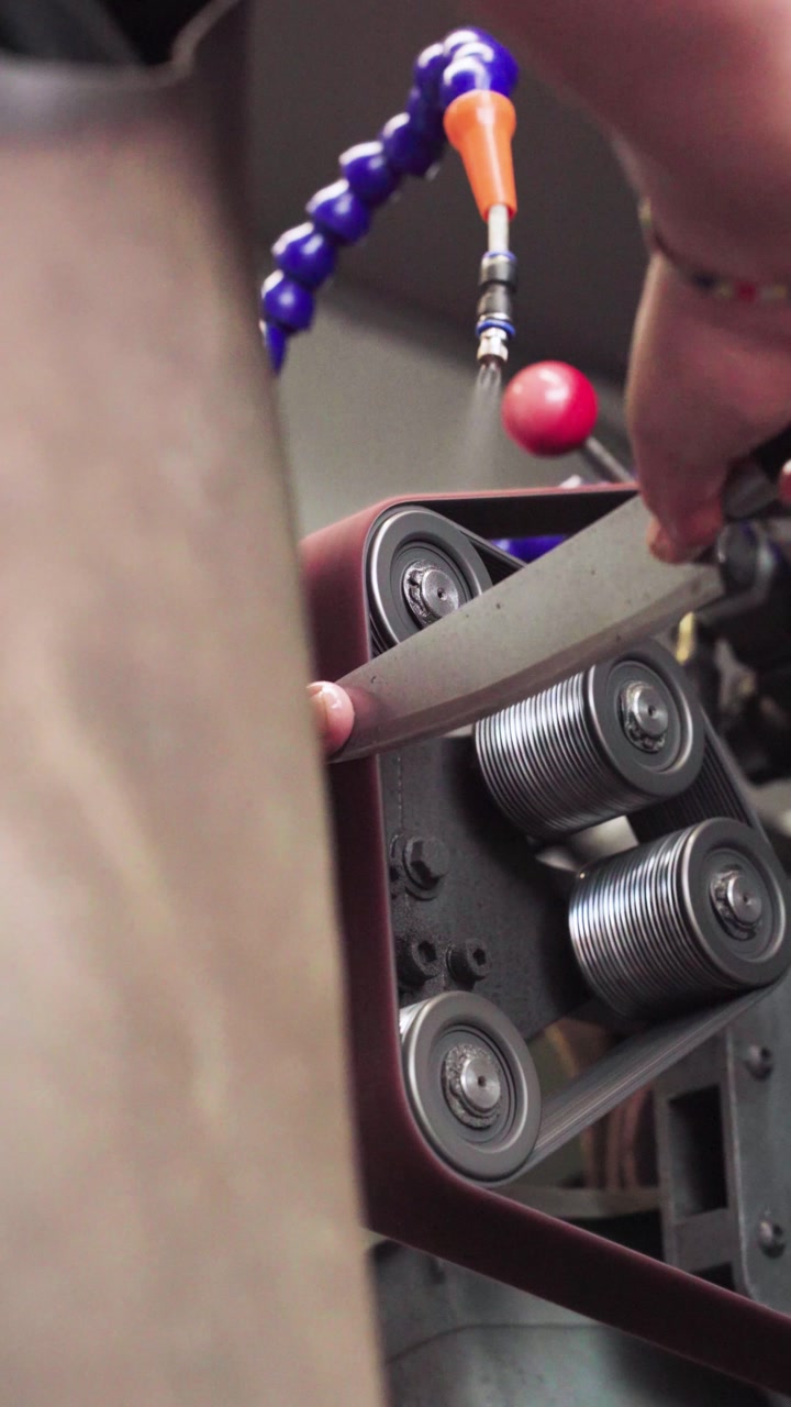 Vertical shot knife sharpening machine in operation in Malaysia. Close-up of belt system and mechanical components refining blade edges, highlighting industrial process and precision engineering. UHD.