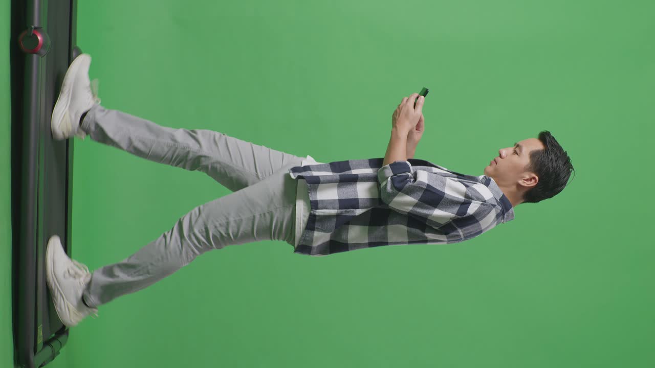 Side View Full Body Of Asian Man Using Mobile Phone While Walking On Green Screen In The Studio