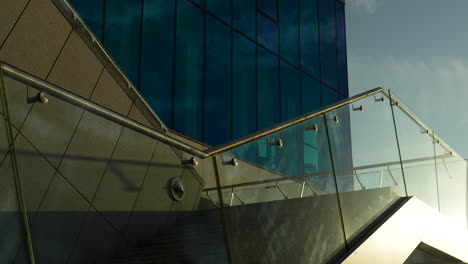 Edificio-Moderno-Con-Ventanas-Tintadas-De-Azul-Y-Elegantes-Barandillas-De-Vidrio-Bajo-Un-Cielo-Iluminado-Por-El-Sol