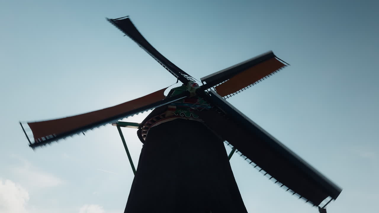 Traditional Dutch windmill's silhouette with its sails rotating in motion blur against a clear blue sky