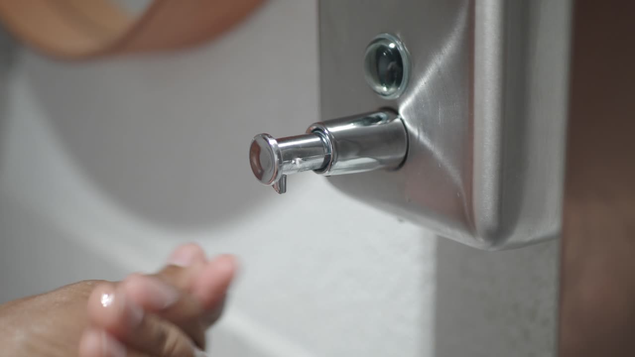 A person using a hand soap dispenser in a bathroom